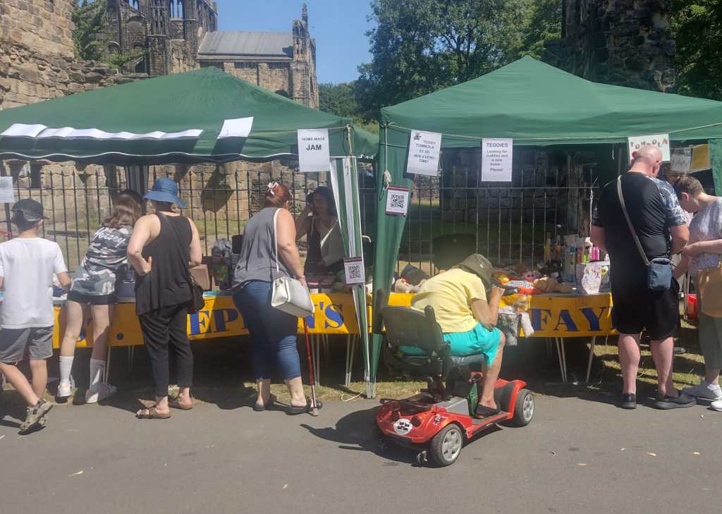 St Stephen's two festival stalls, with many people milling in front of them, and Kirkstall abbey in the background.