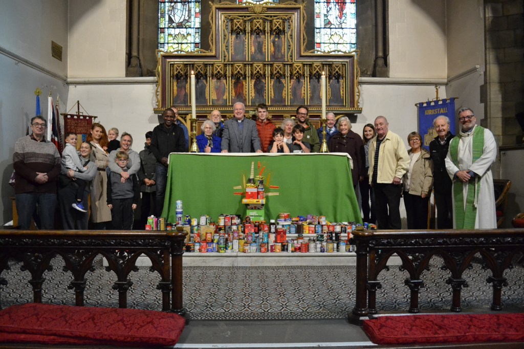 A large group of people standing at the alter of a church with lots of tinned foods spread out around them